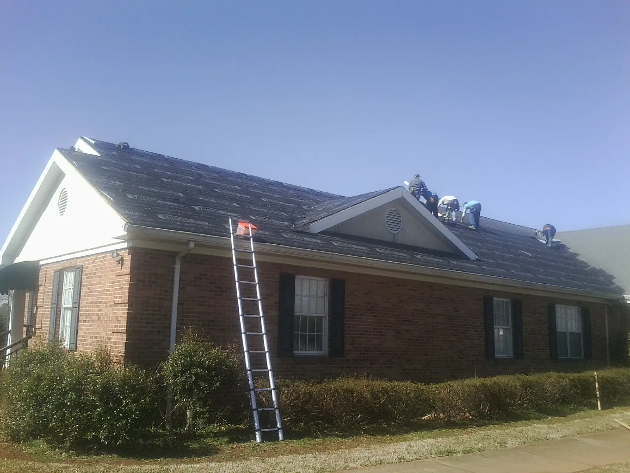 Crew tearing shingles off a brick ranch roof with a ladder set — Emergency Roof Repair work by our crew in Olney