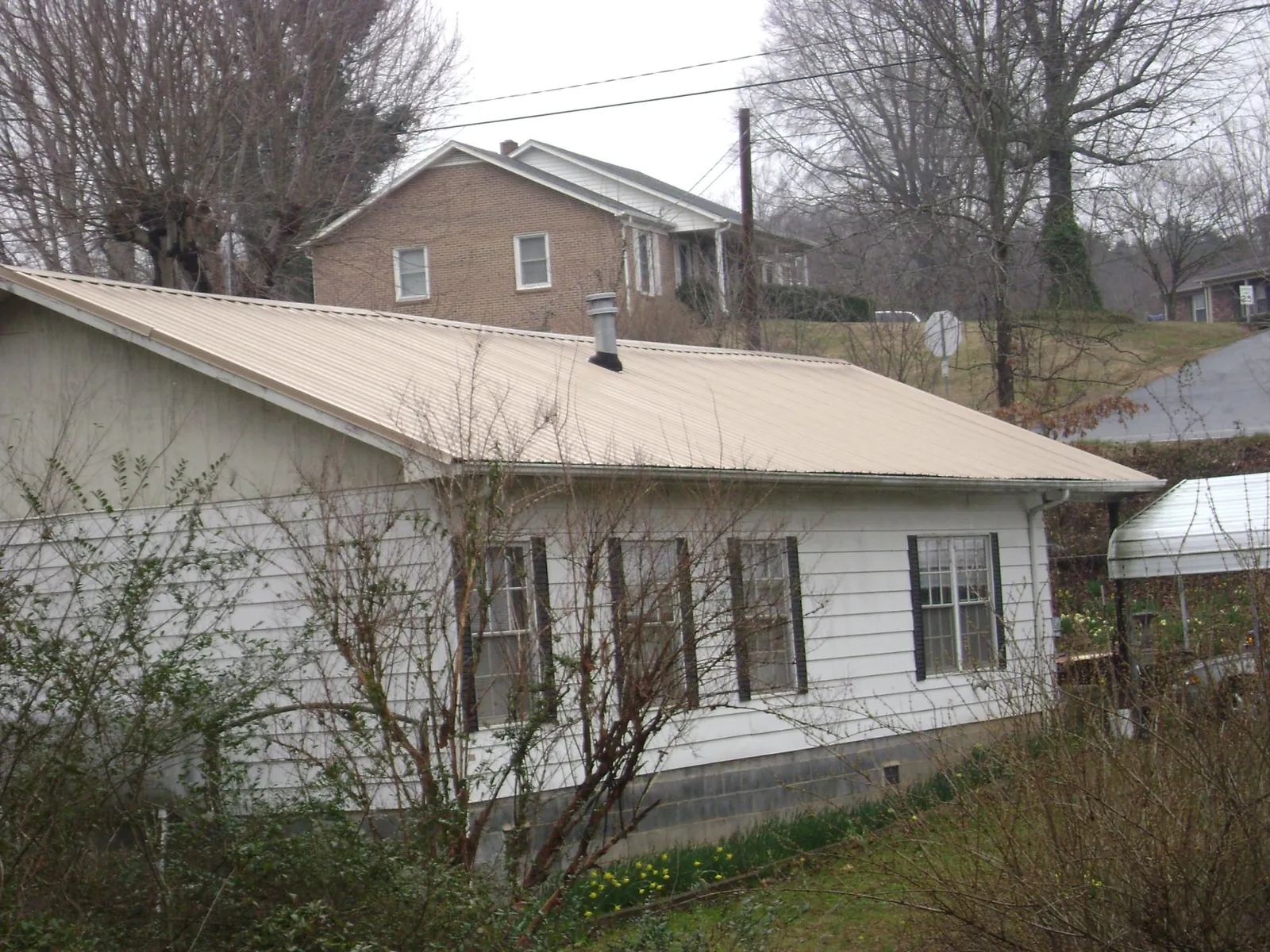 Tan metal roof on a white sided house set into a hillside — Commercial Roofing by Roofing Brothers in Olney